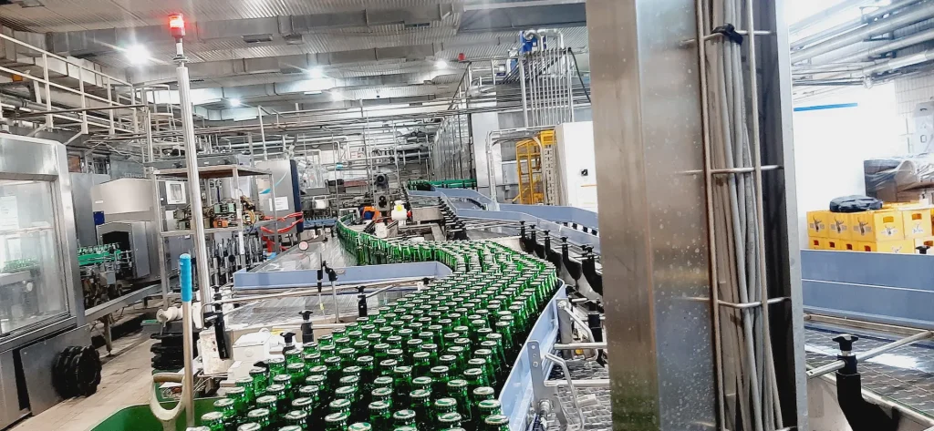 Redovi zelenih staklenih flaša na krivini akumulacionog transportera u fabrici.